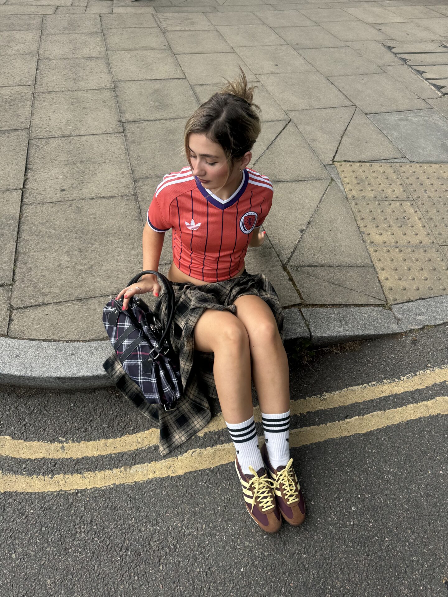 @bailliejones wearing the brown adidas SL 72 with white and black adidas socks, a checked brown midi skirt, a red Scotland top, and a checked handbag.